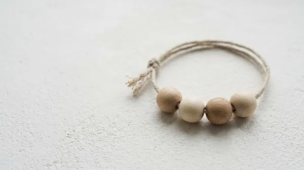 Four wooden beads in two tones threaded on a loop of natural twine on a white plaster surface, illustrating the 4 Cs of feedback as four linked steps