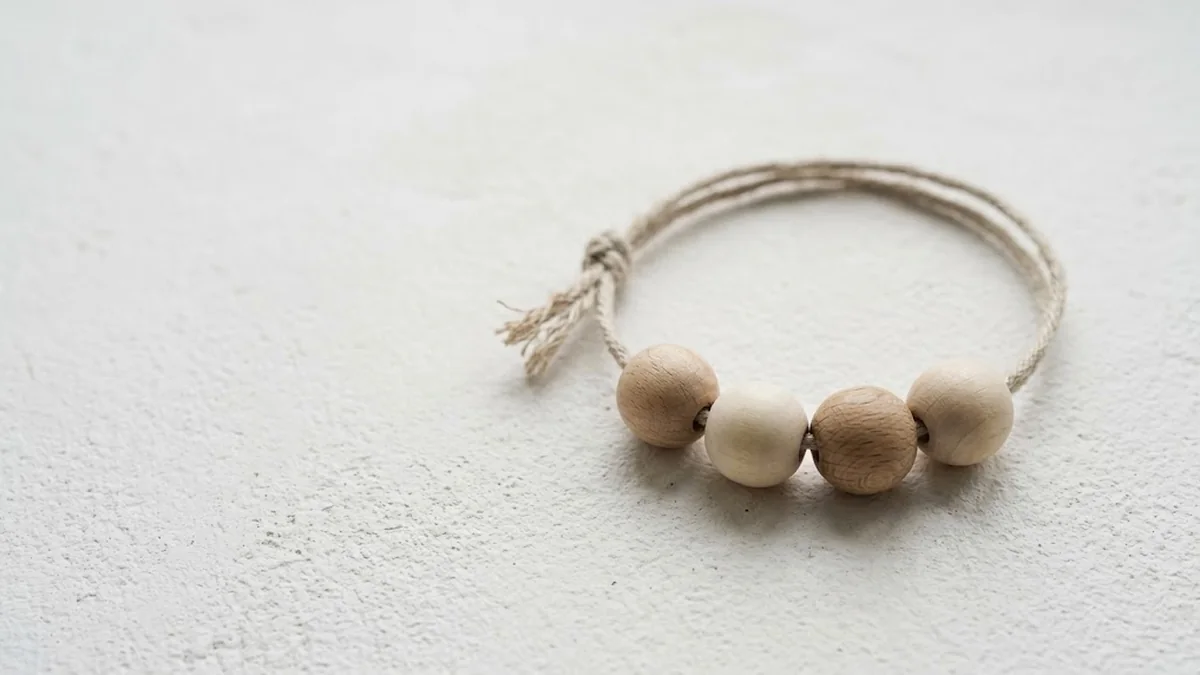 Four wooden beads in two tones threaded on a loop of natural twine on a white plaster surface, illustrating the 4 Cs of feedback as four linked steps