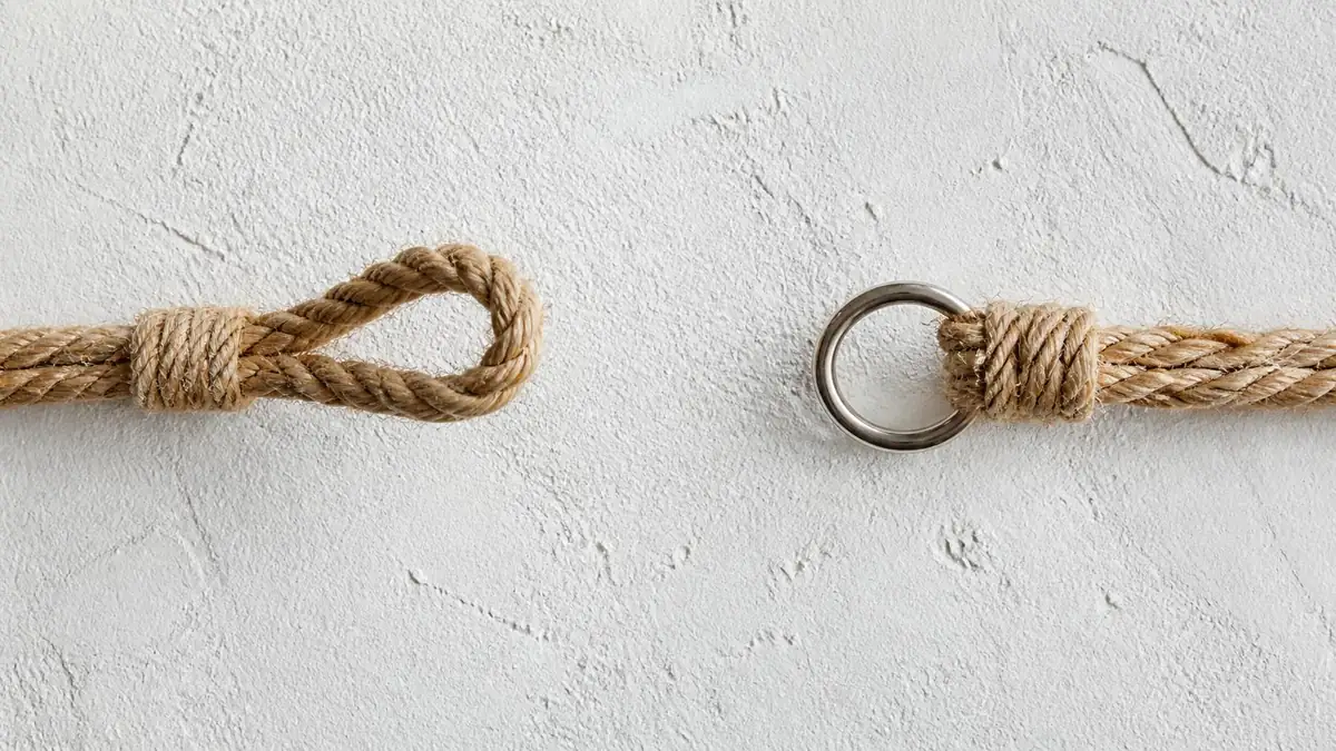 Two ends of a jute rope facing each other across a gap on a white plaster wall, one ending in a loop and the other in a steel ring, illustrating accountability statistics on the gap between how leaders rate themselves and how their managers rate them