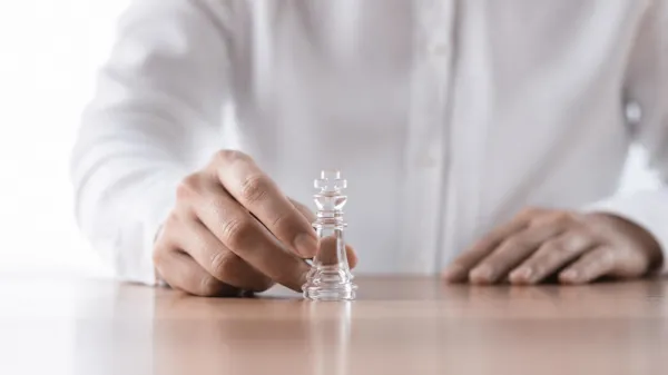 A hand carefully moving a clear glass king chess piece on a table, symbolizing the strategic moves that keep AI leadership rollouts from stalling