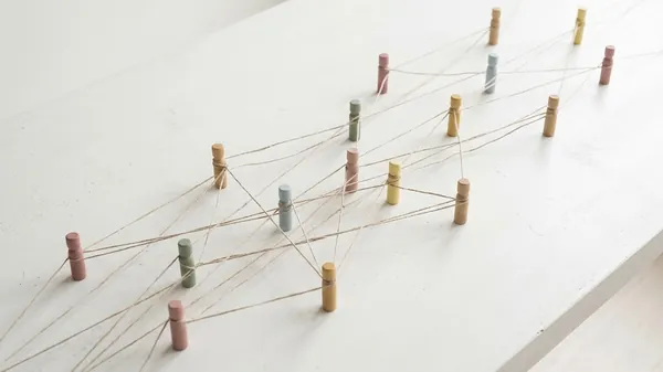 Pastel wooden pegs standing on a white table and linked to one another by a web of twine, illustrating CEO networking groups and the connections between members