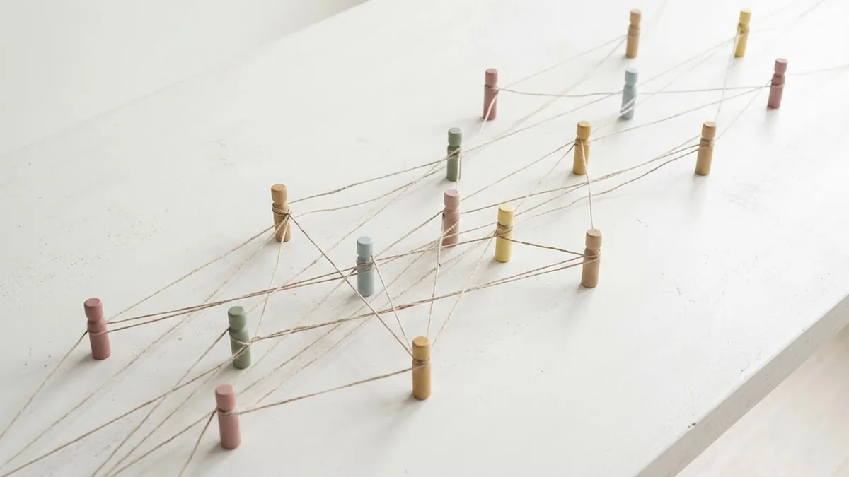 Pastel wooden pegs standing on a white table and linked to one another by a web of twine, illustrating CEO networking groups and the connections between members