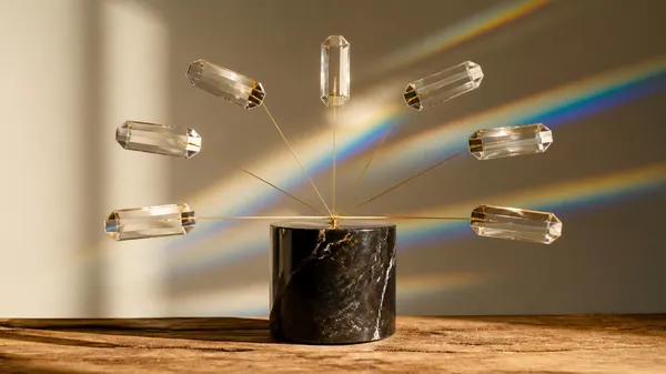 Seven clear crystal prisms fanned out on thin brass rods from one black marble base, catching sunlight and casting rainbows on the wall, illustrating a manager and the direct reports in their span of control
