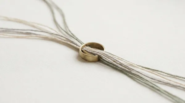 Loose strands of linen thread in cream, grey and sage gathered through a single brass ring on white fabric, illustrating the EOS Integrator who pulls the functions of a company together