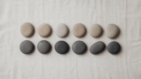 Twelve smooth stones on natural linen in two rows, six pale and six dark, representing the pros and cons of running a company on the EOS Traction system