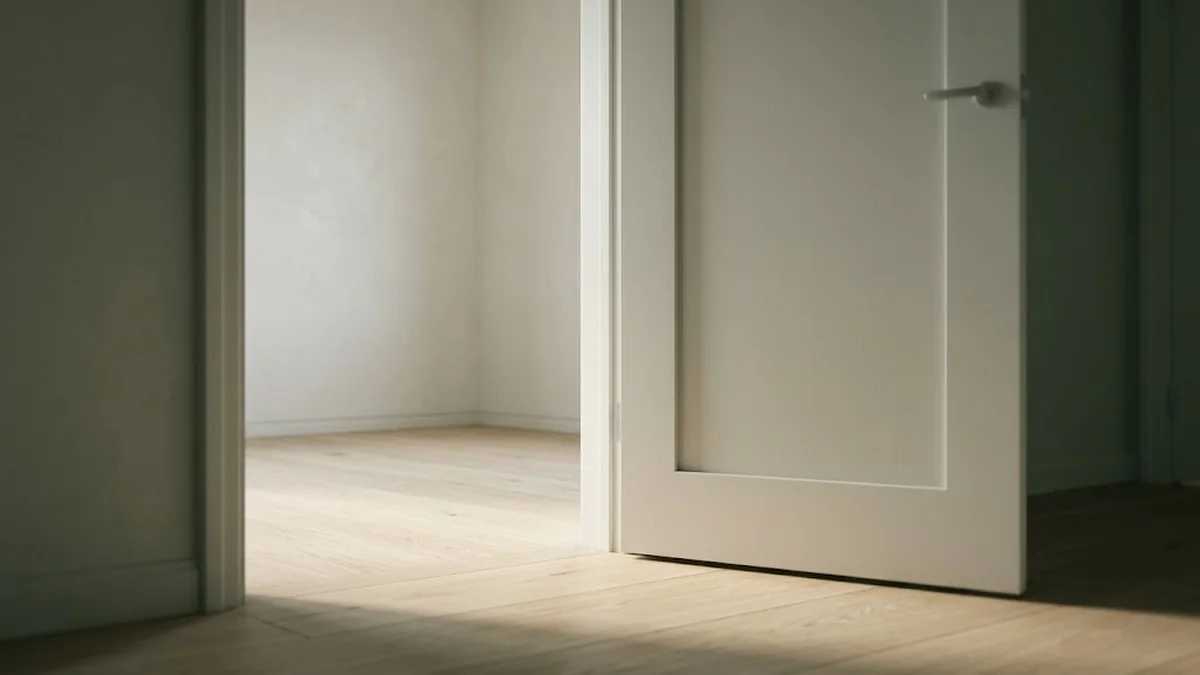 A white door standing open onto an empty sunlit room with a pale wood floor, illustrating how to fire someone with a clear and respectful exit