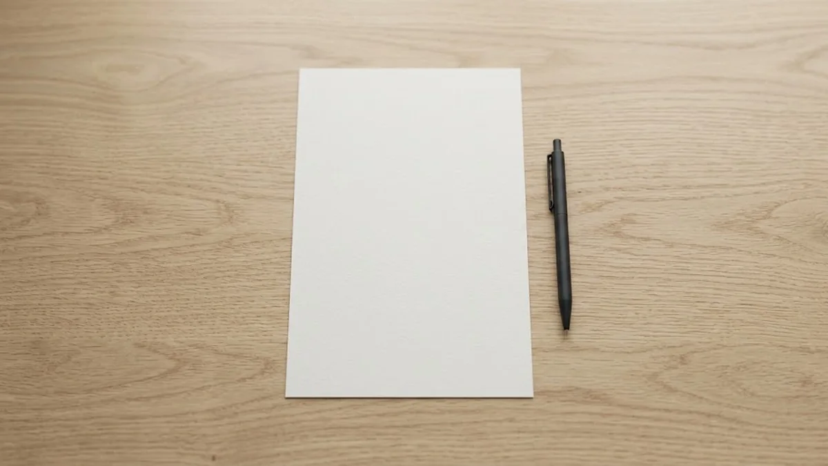 A blank sheet of white paper with a black pen beside it on a pale oak desk seen from above, illustrating a manager about to write a performance improvement plan