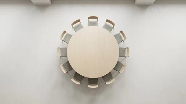 Overhead view of a round pale oak meeting table ringed by matching chairs in a bright empty room, illustrating the weekly Level 10 Meeting of a leadership team