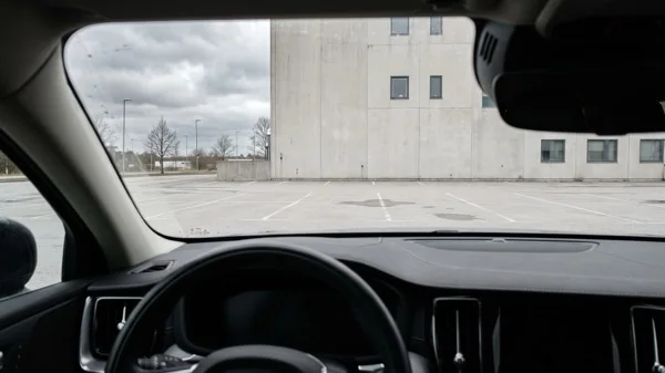 The view from inside a parked car looking out at an empty lot and a plain concrete office building under a grey sky, illustrating the reflective space of one-on-one executive coaching for senior leaders