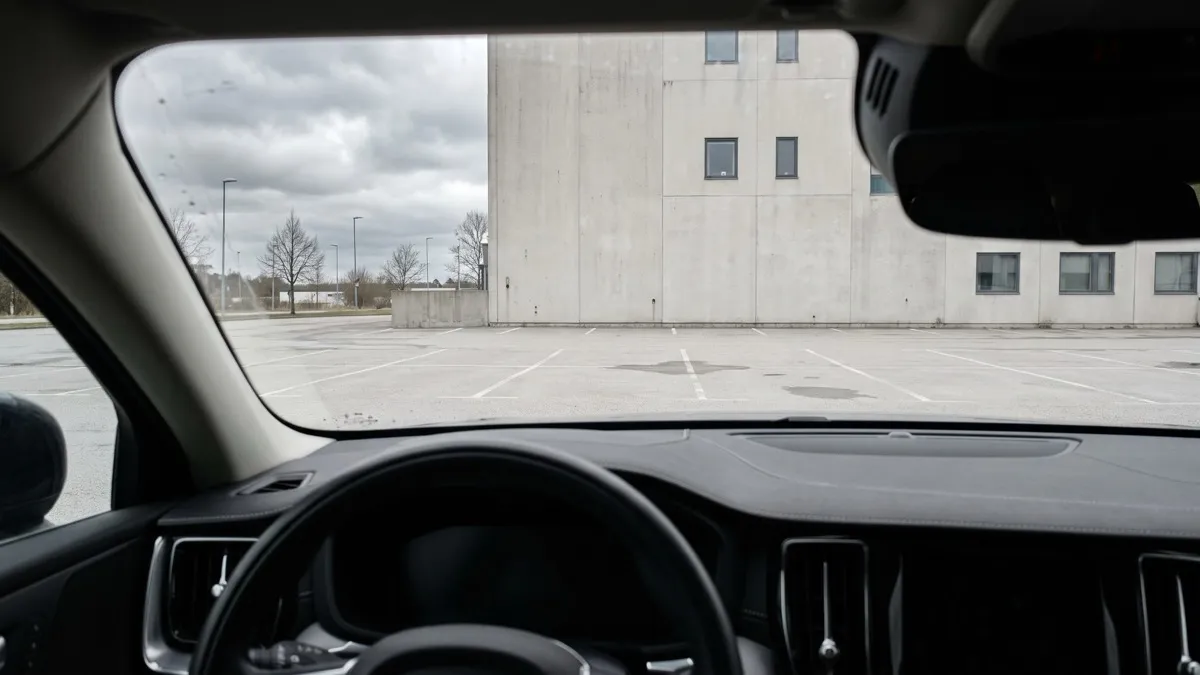 The view from inside a parked car looking out at an empty lot and a plain concrete office building under a grey sky, illustrating the reflective space of one-on-one executive coaching for senior leaders