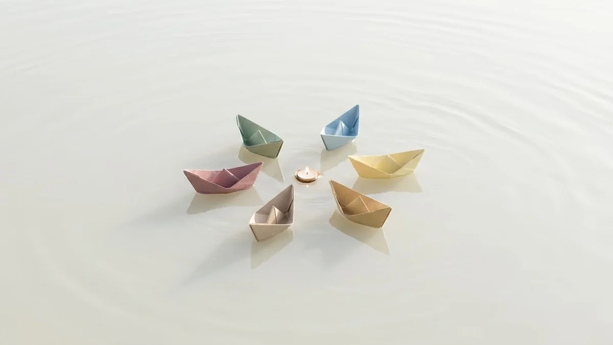 Six pastel paper boats floating in a ring around a small lit candle on still water, illustrating peer advisory groups gathered around one shared question
