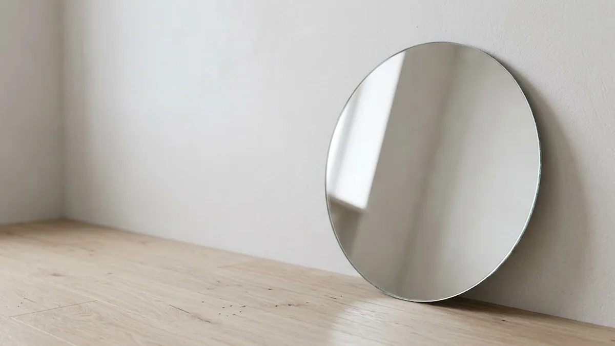 A round frameless mirror leaning against a white wall on a pale oak floor, reflecting soft window light, illustrating protreptic as the leadership dialogue that turns a leader back toward the values they live by