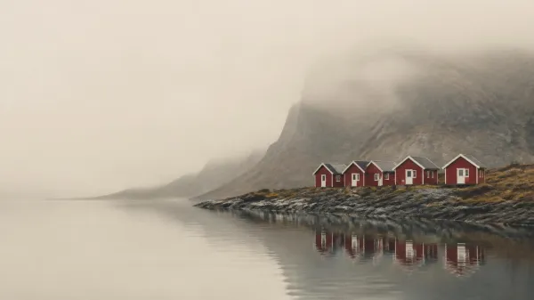 Row of identical red wooden cabins along a misty fjord shore beneath a mountain, evoking the calm egalitarian Scandinavian leadership style