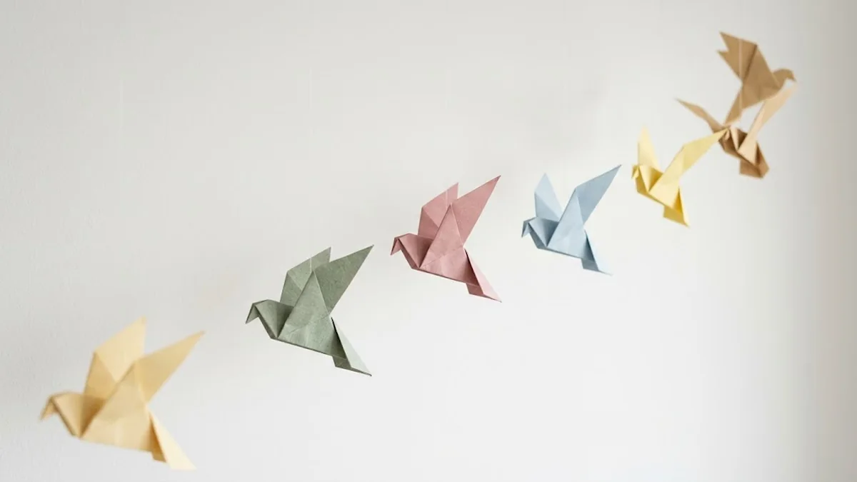 Six origami paper birds in pastel yellow, sage, pink, blue and tan hanging in a rising diagonal line against a white wall, illustrating the types of followership and the different followers a company produces